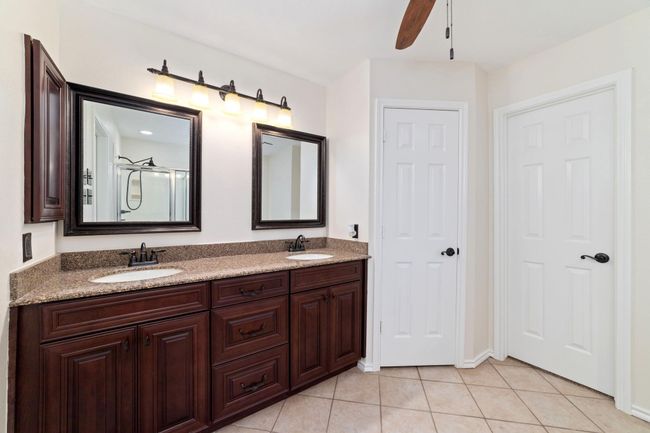 Open and airy primary bathroom featuring a double vanity with sleek quartz countertops, rich cherrywood finishes. | Image 22