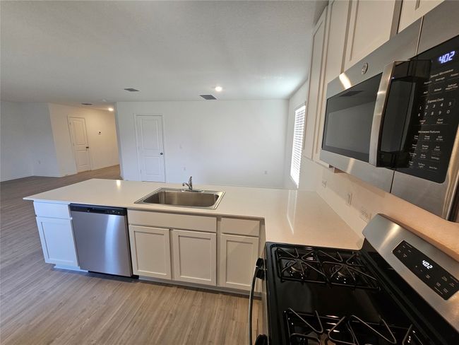 Kitchen featuring a sink, stainless steel appliances, light wood-type flooring, a peninsula, and light countertops | Image 8
