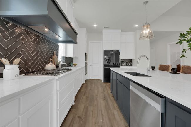 Kitchen featuring white cabinets, a sink, extractor fan, backsplash, and appliances with stainless steel finishes | Image 11