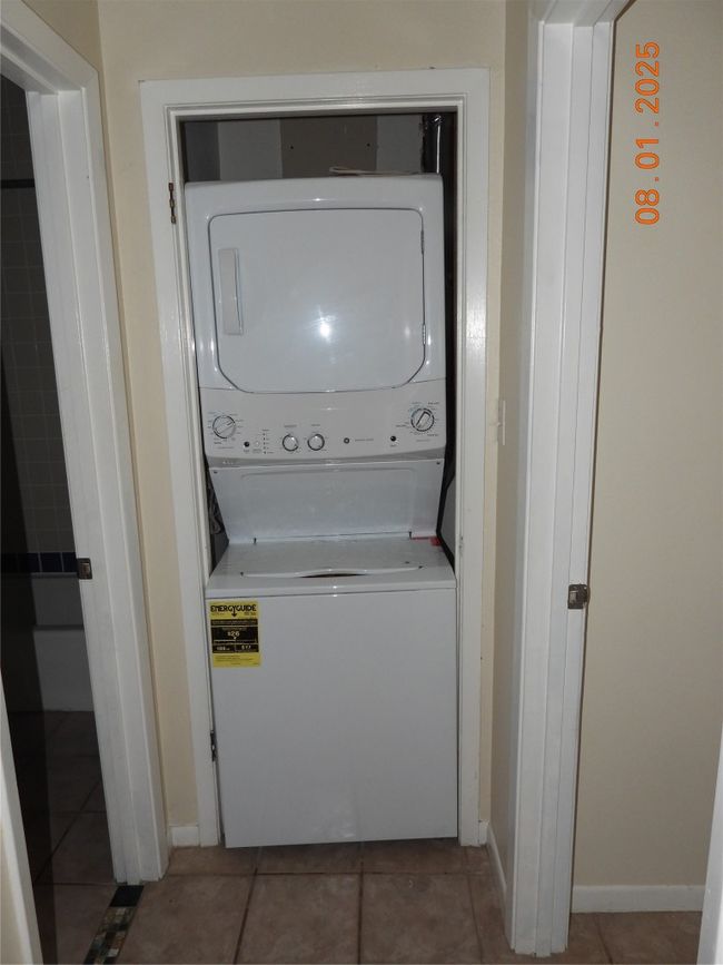 Laundry room with tile patterned flooring and stacked washing machine and dryer | Image 12