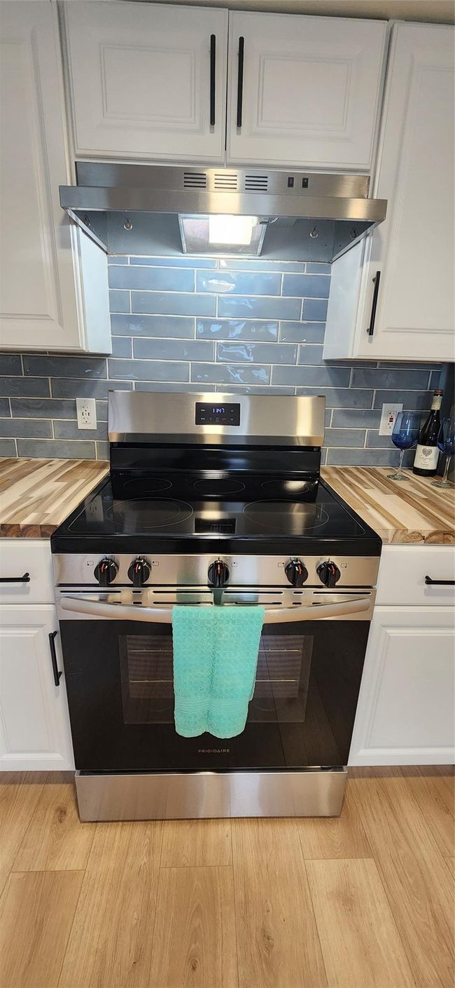Kitchen with ventilation hood, stainless steel range with electric stovetop, white cabinets, wood counters, and decorative backsplash | Image 6