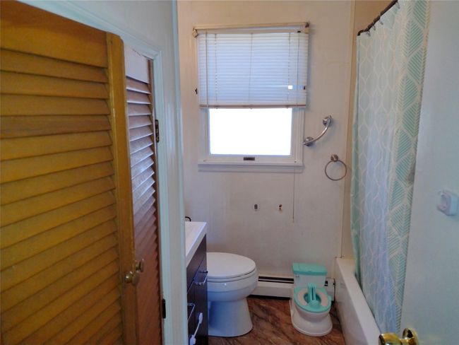 Bathroom with vanity, wood finished floors, baseboard heating, toilet, and shower / tub combo with curtain | Image 21