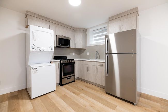Kitchen featuring stainless steel appliances, stacked washing machine and dryer, light countertops, a sink, and light wood-style flooring | Image 33