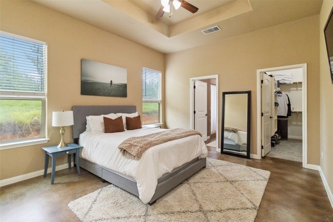 Bedroom featuring baseboards, finished concrete flooring, a walk in closet, a raised ceiling, and a closet | Image 21