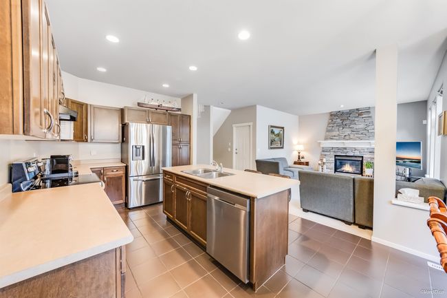 Kitchen featuring a sink, under cabinet range hood, open floor plan, stainless steel appliances, and light countertops | Image 8