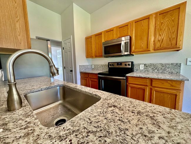 Kitchen featuring stainless steel appliances, brown cabinetry, and light stone counters | Image 8