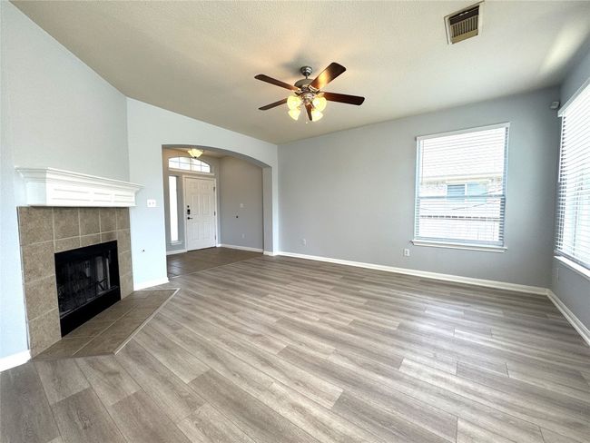 Unfurnished living room featuring a ceiling fan, wood finished floors, arched walkways, a fireplace, and a textured ceiling | Image 5