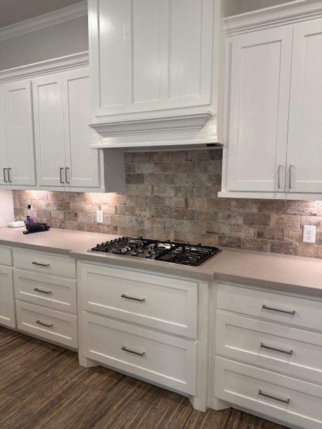 Kitchen featuring white cabinets, light countertops, stainless steel gas cooktop, ornamental molding, and exhaust hood | Image 11