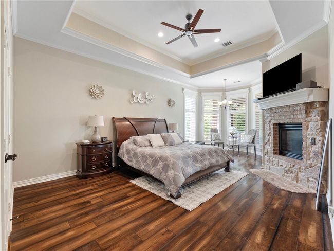 Bedroom with wood finished floors, a raised ceiling, a chandelier, crown molding, and a stone fireplace | Image 20