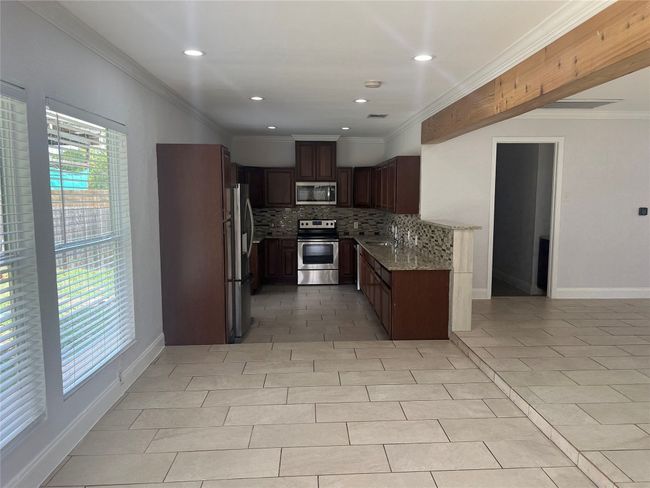 Kitchen with stainless steel appliances, backsplash, ornamental molding, light tile patterned floors, and light stone countertops | Image 8
