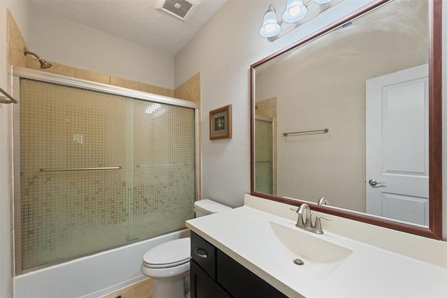 This full upstairs bathroom features a sleek vanity with modern fixtures, a large framed mirror, and a tiled tub/shower combo with sliding glass doors. Conveniently located to serve secondary bedrooms and the gameroom. | Image 20