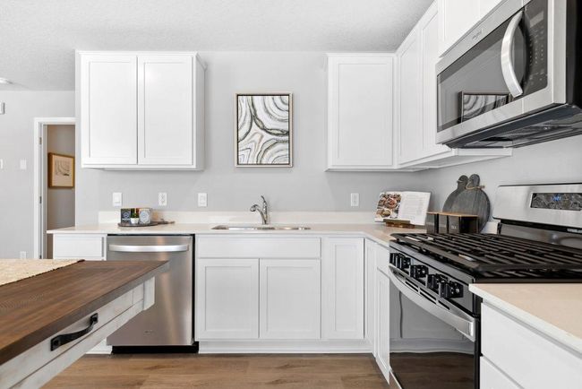 Stainless steel appliances, stone counters, and LVP flooring create a worry free home! Another similar kitchen layout, home will feature a built in island. Photo of a similar layout model home, layout and colors will vary. | Image 4