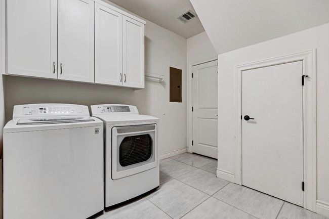 Washroom featuring washer and dryer, cabinet space, light tile patterned flooring, and electric panel | Image 23