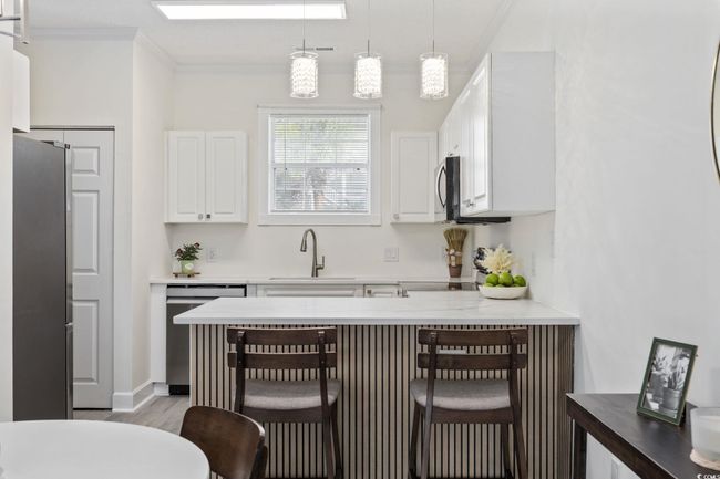 Kitchen with appliances with stainless steel finishes, crown molding, a peninsula, white cabinetry, and a kitchen breakfast bar | Image 13
