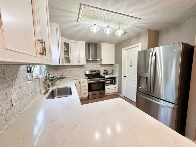 Kitchen featuring appliances with stainless steel finishes, wall chimney range hood, decorative backsplash, light stone countertops, and white cabinets | Image 5