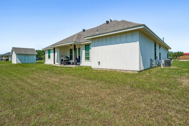 Back of property featuring central AC unit, a yard, a shingled roof, and board and batten siding | Image 23