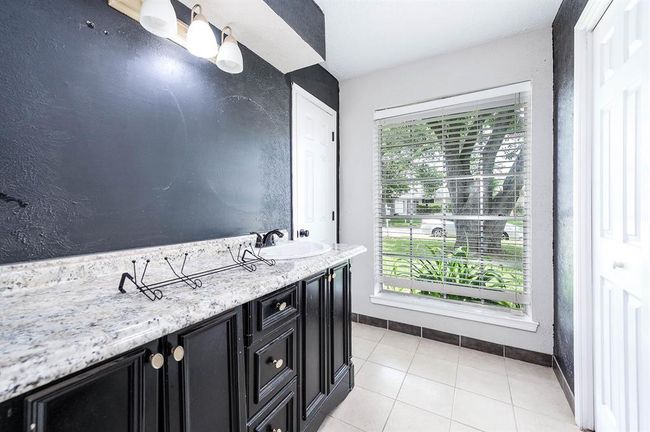 This bathroom features a double sink vanity with a granite countertop and dark cabinetry. It has a large window with blinds, providing natural light and a view of the outside. The space is accented with dark and light wall colors, and the floor is tiled. | Image 20