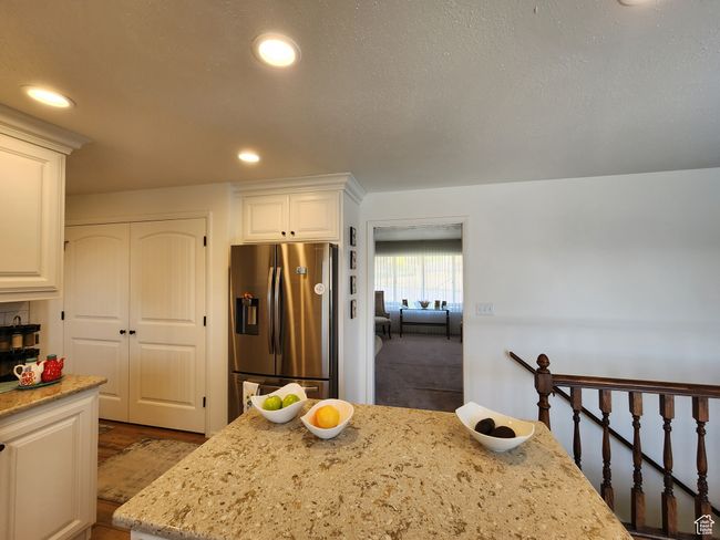 Kitchen with light stone countertops, wood finished floors, stainless steel fridge with ice dispenser, white cabinets, and recessed lighting | Image 16