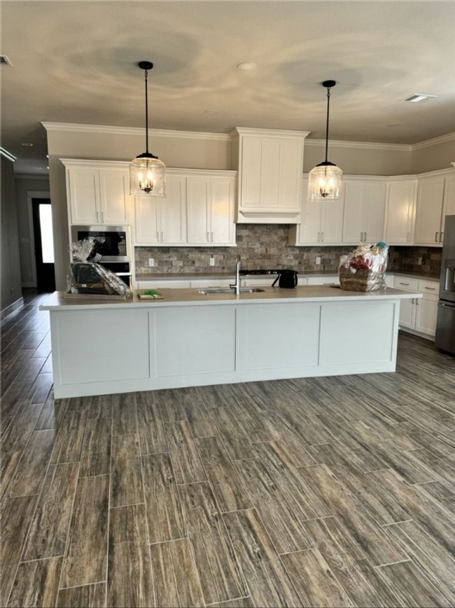 Kitchen featuring crown molding, white cabinetry, refrigerator with ice dispenser, tasteful backsplash, and decorative light fixtures | Image 7