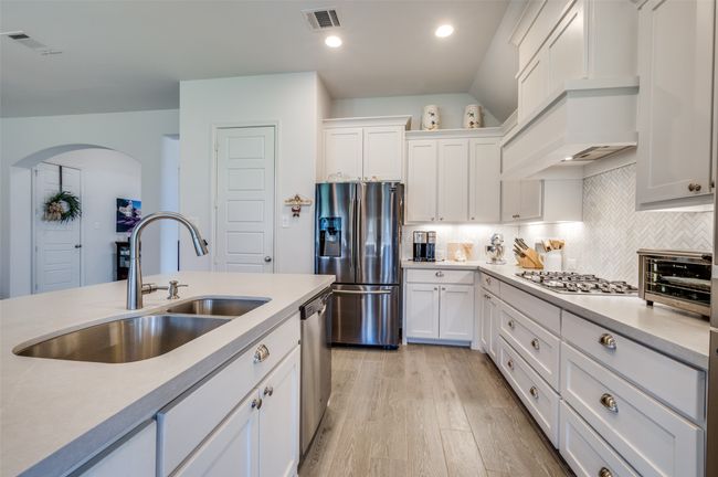 Kitchen featuring stainless steel appliances, a sink, arched walkways, light wood-style flooring, and light countertops | Image 12