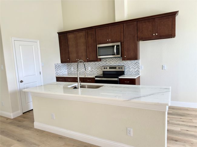 Kitchen featuring appliances with stainless steel finishes, a sink, light wood-style floors, baseboards, and a high ceiling | Image 38