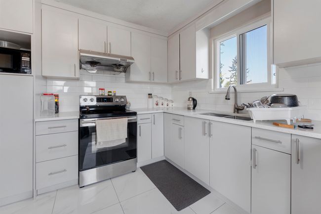 Kitchen with a sink, under cabinet range hood, decorative backsplash, light countertops, and electric range | Image 12