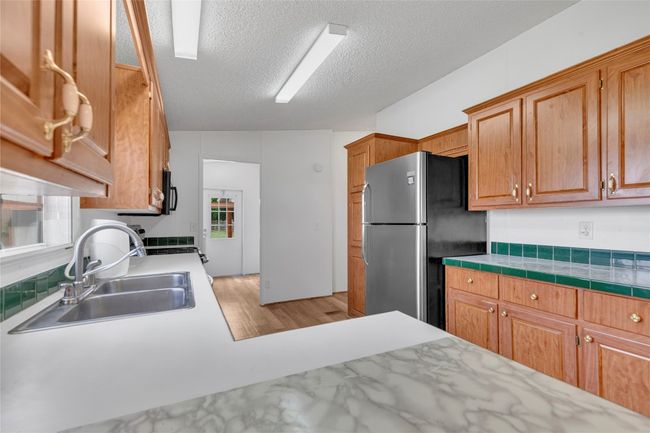 Kitchen with freestanding refrigerator, light wood finished floors, light countertops, a textured ceiling, and brown cabinets | Image 15