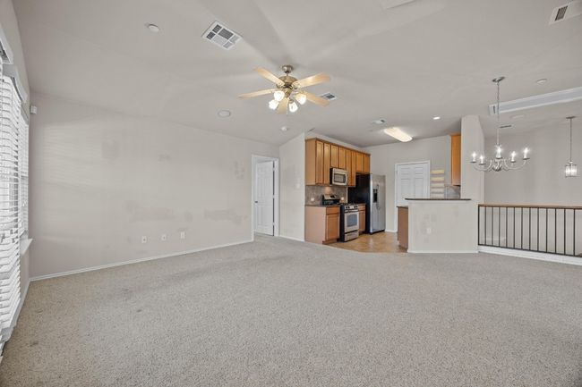 Unfurnished living room featuring ceiling fan with notable chandelier, visible vents, and light colored carpet | Image 10