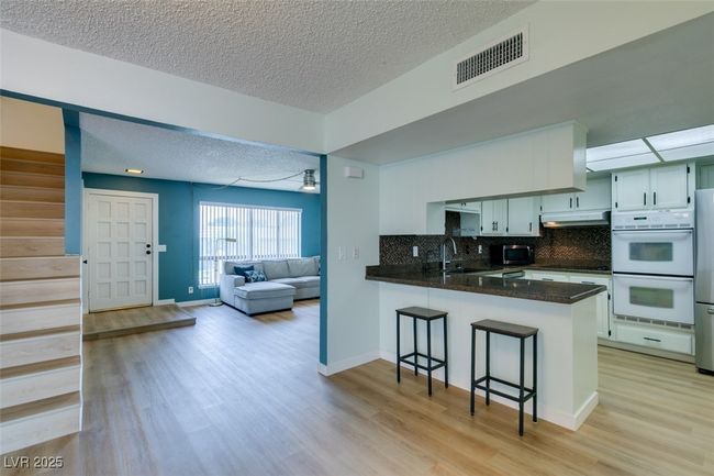 Kitchen featuring double oven, under cabinet range hood, a peninsula, a textured ceiling, and a breakfast bar | Image 23