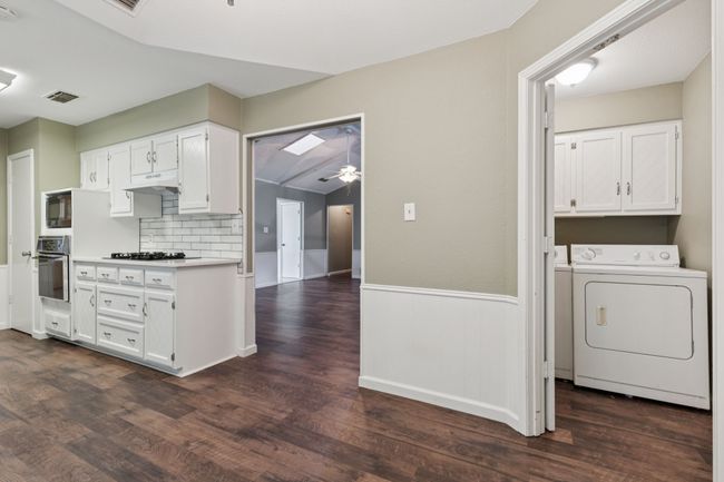 Kitchen featuring washer / dryer, stainless steel oven, dark wood-type flooring, white cabinetry, and wainscoting | Image 15