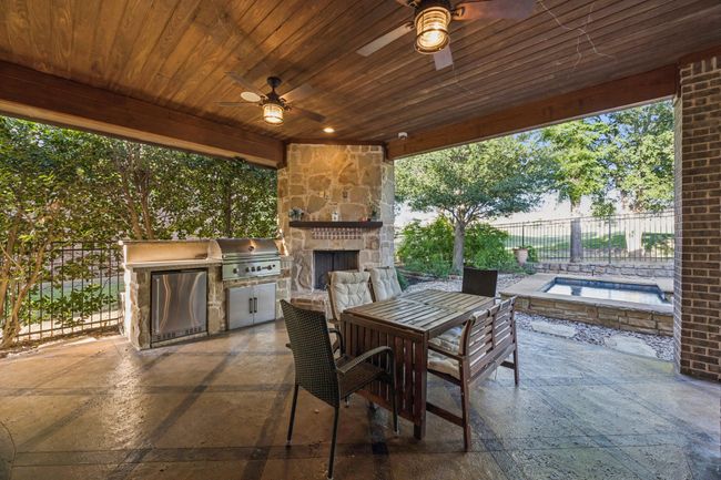 View of patio featuring an outdoor stone fireplace, ceiling fan, exterior kitchen, and outdoor dining area | Image 28