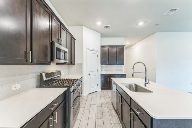Kitchen featuring appliances with stainless steel finishes, backsplash, an island with sink, dark brown cabinetry, and recessed lighting | Image 5
