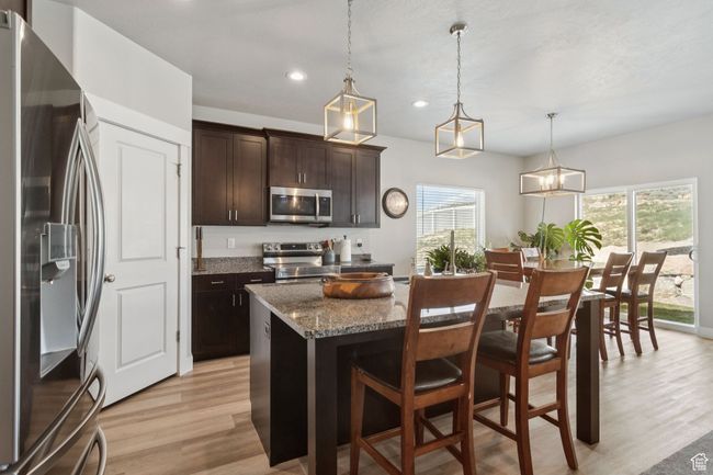 Kitchen featuring stainless steel appliances, light wood-type flooring, recessed lighting, a breakfast bar area, and a center island | Image 14