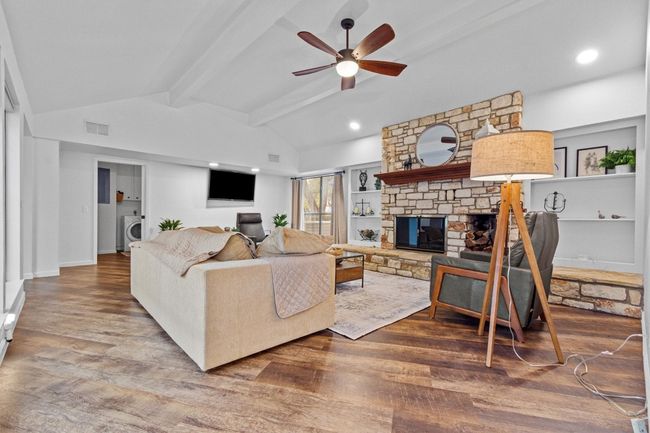 Living room featuring ceiling fan, a fireplace, washer / dryer, lofted ceiling with beams, and built in shelves | Image 9