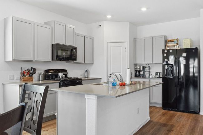 Kitchen with black appliances, dark wood finished floors, a sink, and a center island with sink | Image 9