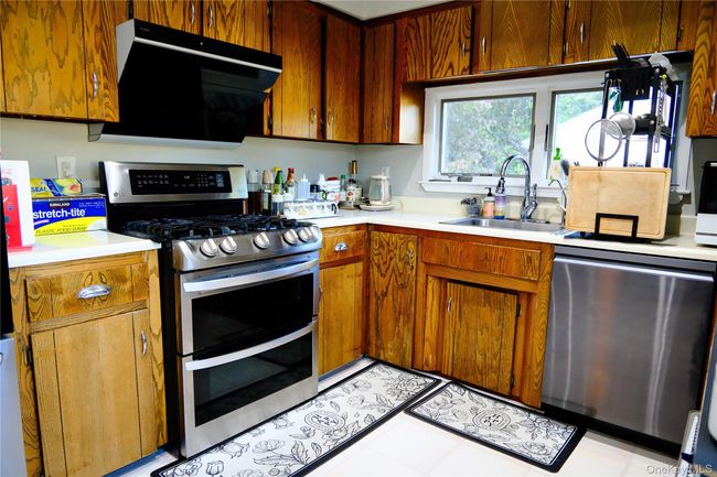 Kitchen with appliances with stainless steel finishes, light countertops, range hood, brown cabinetry, and light tile patterned floors | Image 16