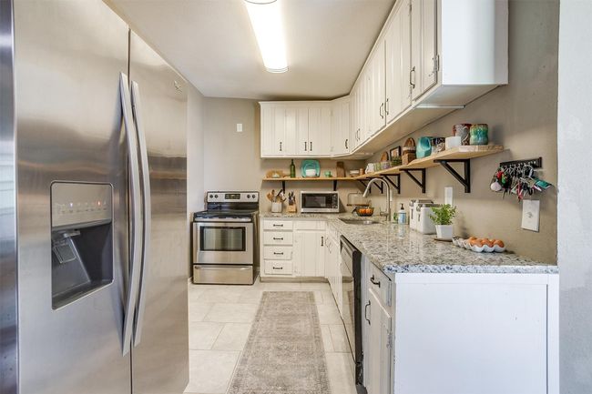 Kitchen featuring appliances with stainless steel finishes, open shelves, light tile patterned floors, and white cabinets | Image 8