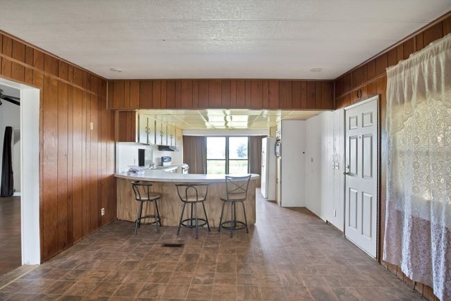 Kitchen with wood walls, a peninsula, a breakfast bar area, light countertops, and brown cabinets | Image 9