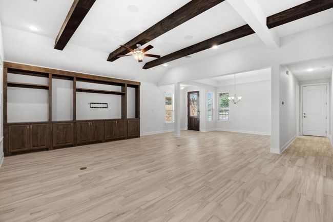 Unfurnished living room featuring beamed ceiling, light wood-style flooring, ceiling fan with notable chandelier, and baseboards | Image 8