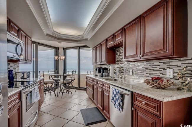 Kitchen featuring appliances with stainless steel finishes, hanging light fixtures, backsplash, a tray ceiling, and sink | Image 8