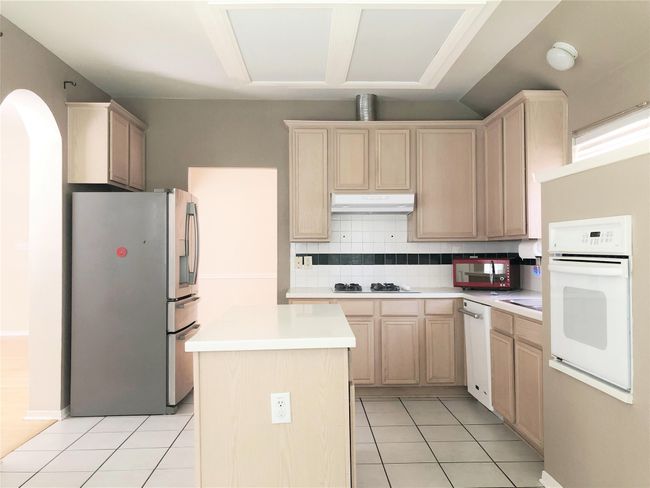 Kitchen featuring white appliances, under cabinet range hood, light brown cabinetry, light countertops, and light tile patterned flooring | Image 6
