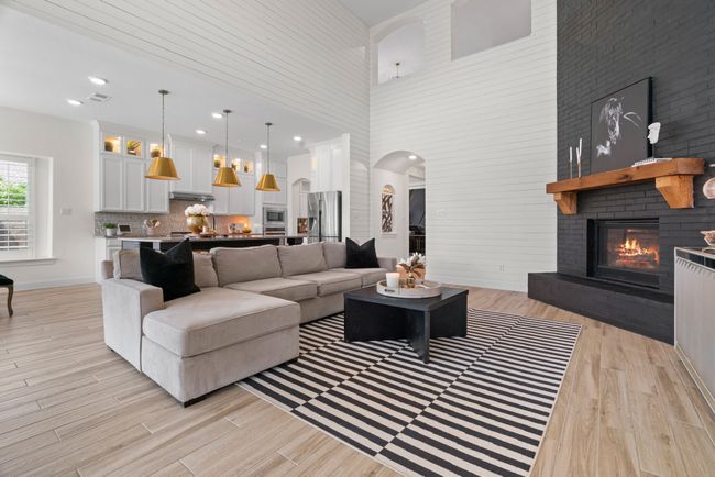 Living room featuring a high ceiling, a brick fireplace, light wood-style flooring, arched walkways, and baseboards | Image 7