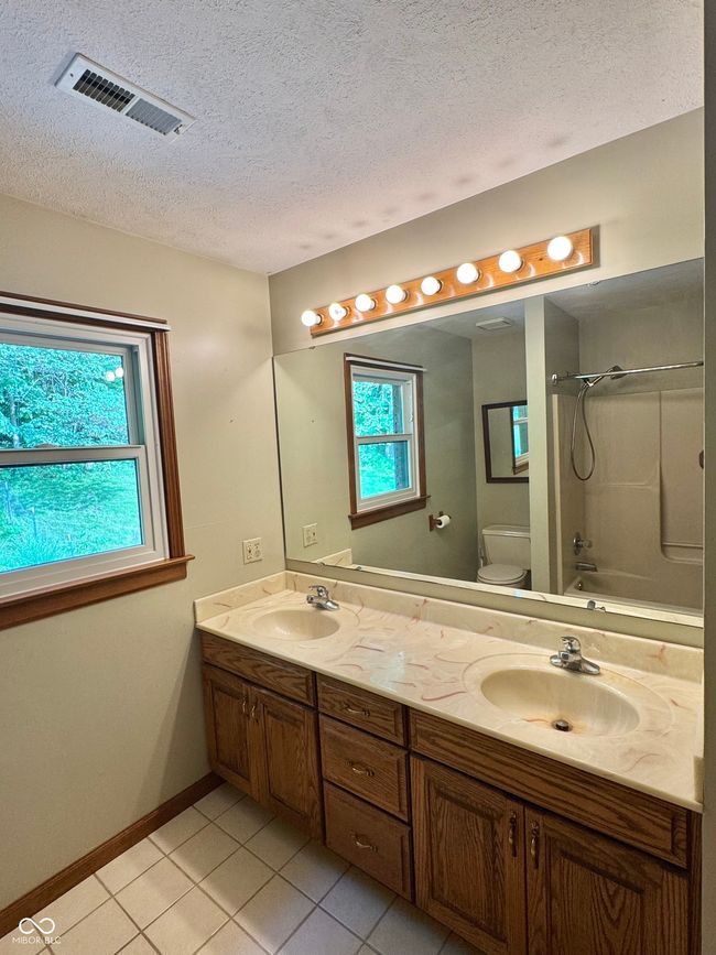 bathroom with tile patterned floors, double vanity, a textured ceiling, toilet, and shower / tub combination | Image 58