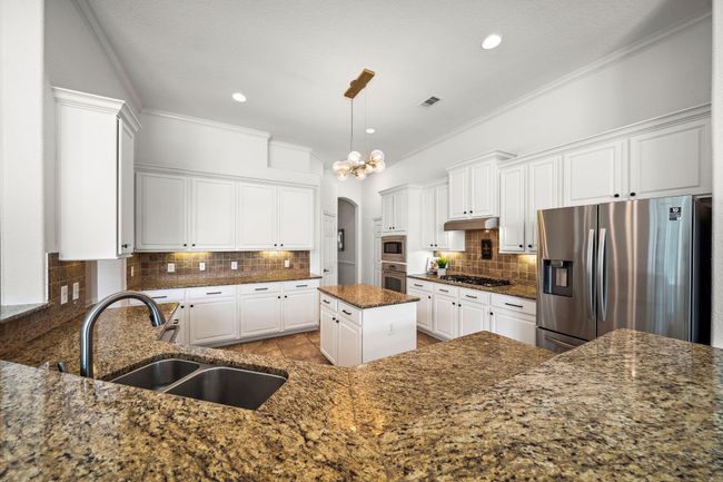 The kitchen features elegant white cabinetry and granite countertops, providing ample storage and workspace. Stainless steel appliances and a central island enhance its functionality, while a breakfast bar offers casual seating, creating an inviting setting for culinary creativity and gatherings. | Image 17