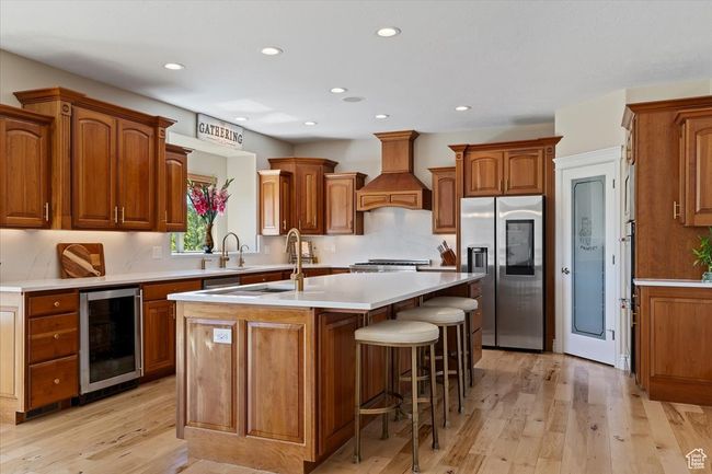 Kitchen featuring stainless steel fridge, beverage cooler, an island with sink, premium range hood, and recessed lighting | Image 13