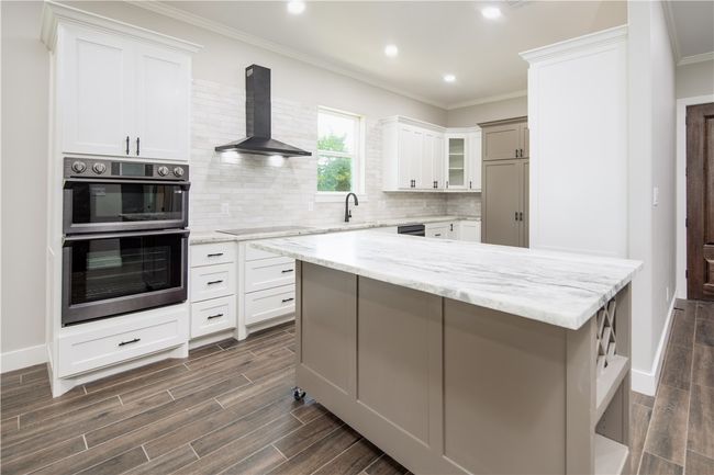 Kitchen featuring double oven, ventilation hood, dark wood-type flooring, crown molding, and recessed lighting | Image 4