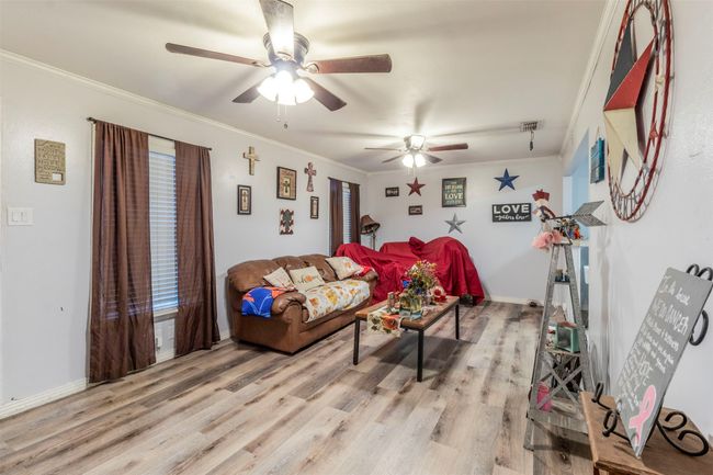 Living room with light wood finished floors, baseboards, a ceiling fan, and ornamental molding | Image 6