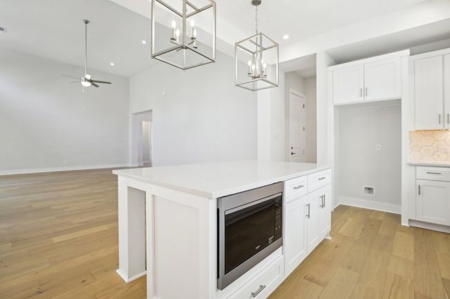 Kitchen with white cabinetry, stainless steel microwave, light wood finished floors, and decorative backsplash | Image 16