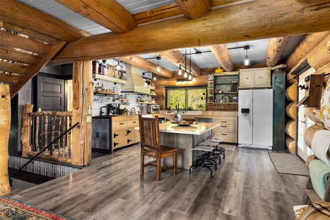 Kitchen featuring white refrigerator with ice dispenser, open shelves, dark wood-style floors, light countertops, and rustic walls | Image 14