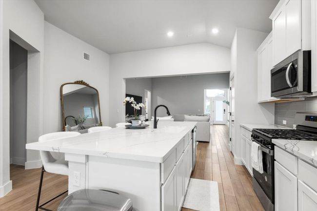 Kitchen with appliances with stainless steel finishes, open floor plan, a kitchen island with sink, white cabinets, and light wood-style flooring | Image 7